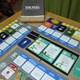 The Poll requires players to draft their manifestoes from policy cards (blue) and mark their influence on constituency cards (green).